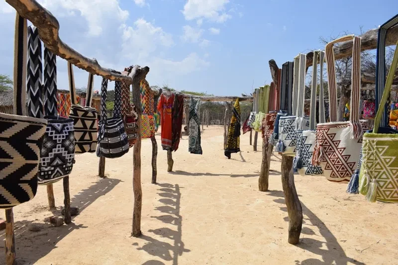 Mochilas Wayuu colgadas en estructura tradicional al aire libre con fondo de desierto claro