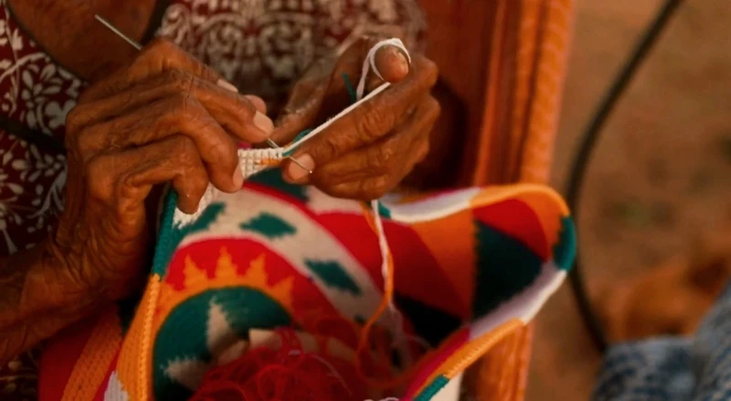 Manos adultas tejiendo con hilo blanco sobre diseño geométrico multicolor