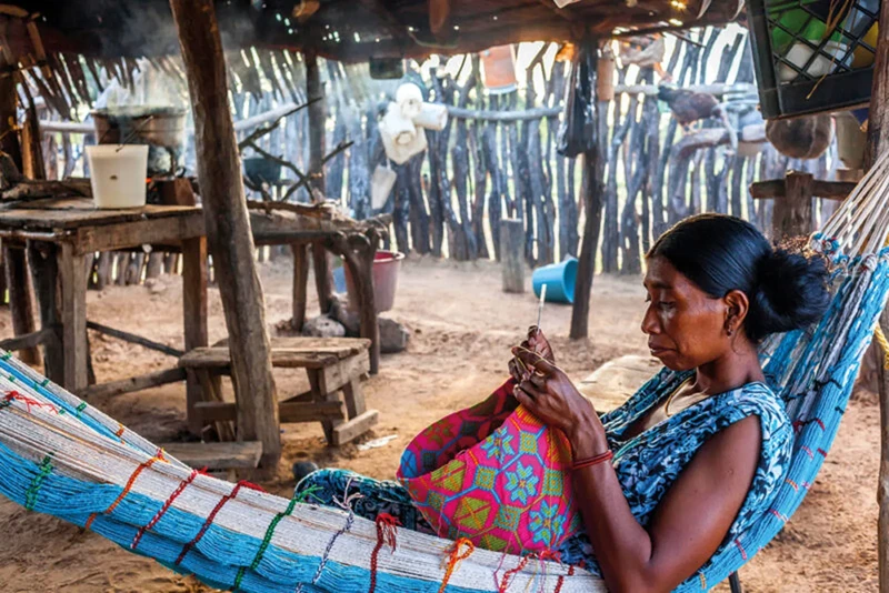 Mujer concentrada en tejido con patrón geométrico desde hamaca tradicional Wayuu