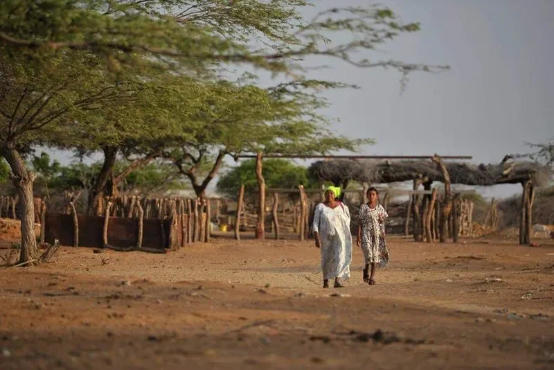 Dos mujeres caminando hacia la entrada de una ranchería tradicional Wayuu