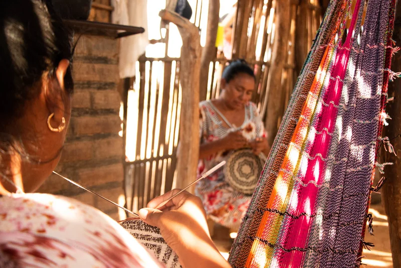 Mujeres tejiendo mochilas en espacio tradicional con chinchorro colorido