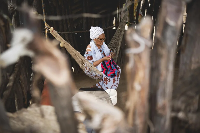 Mujer indígena tejiendo en chinchorro dentro de ranchería tradicional