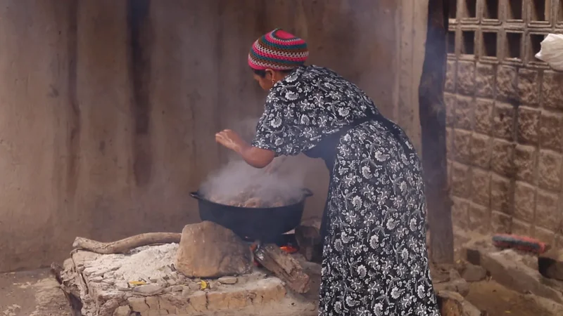 Mujer Wayuu cocinando friche en olla de leña dentro de vivienda tradicional