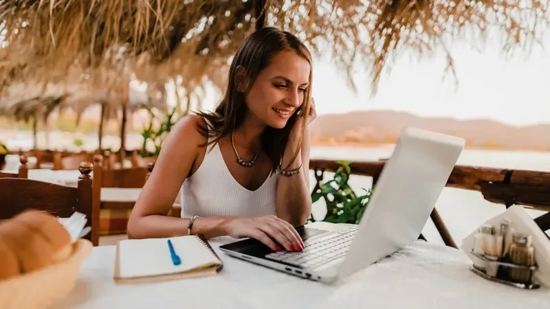 Mujer trabajando online frente al mar en espacio informal con laptop y libreta