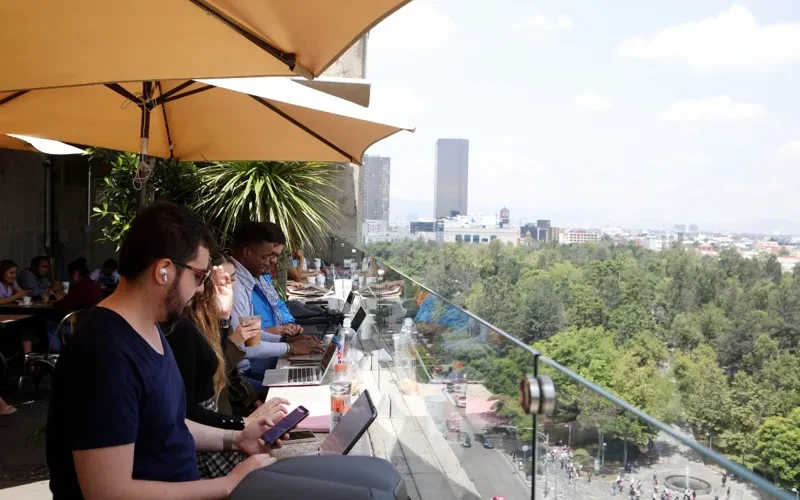 Personas trabajando con laptops en terraza abierta con vista arbolada y sombra natural